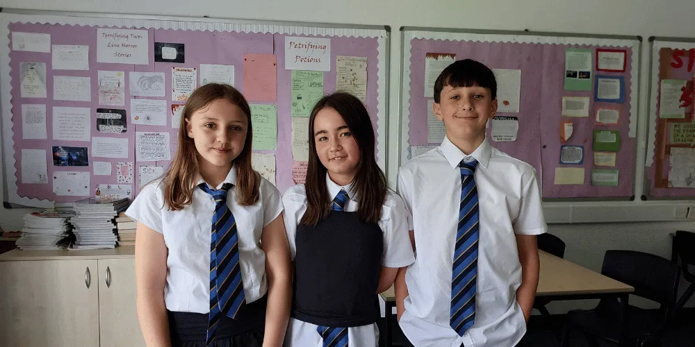 Three children standing in a row, wearing school uniforms.