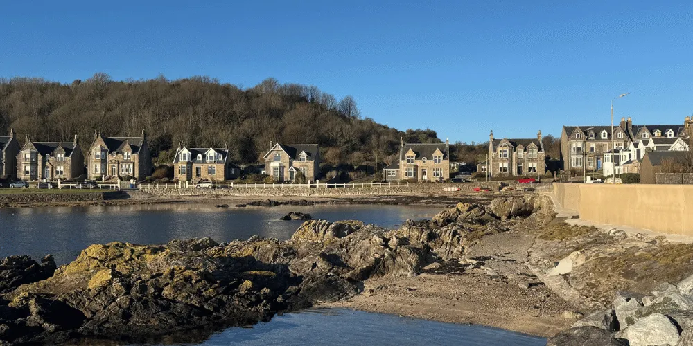 Houses in a coastal town setting, with a beach in the foreground, on a sunny, clear day with blue skies