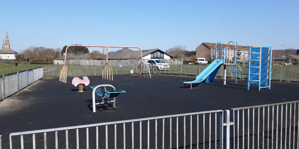 a playpark with various of pieces of equipment, surrounded by a fence