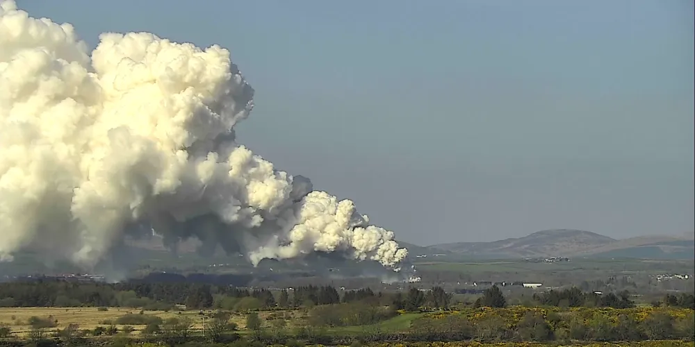 An aerial view of smoke rising from the ground with fields and hills in the distance