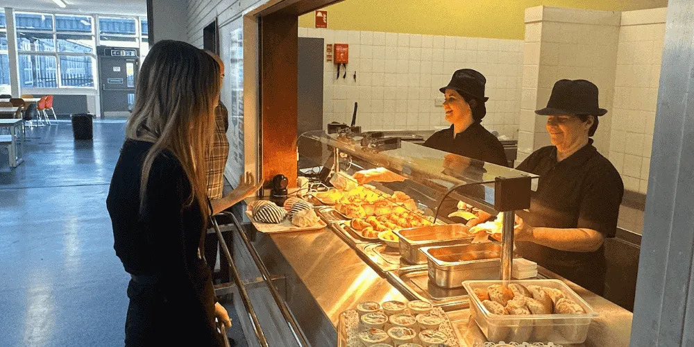 A view of a school dining room with a pupil receiving food from catering staff