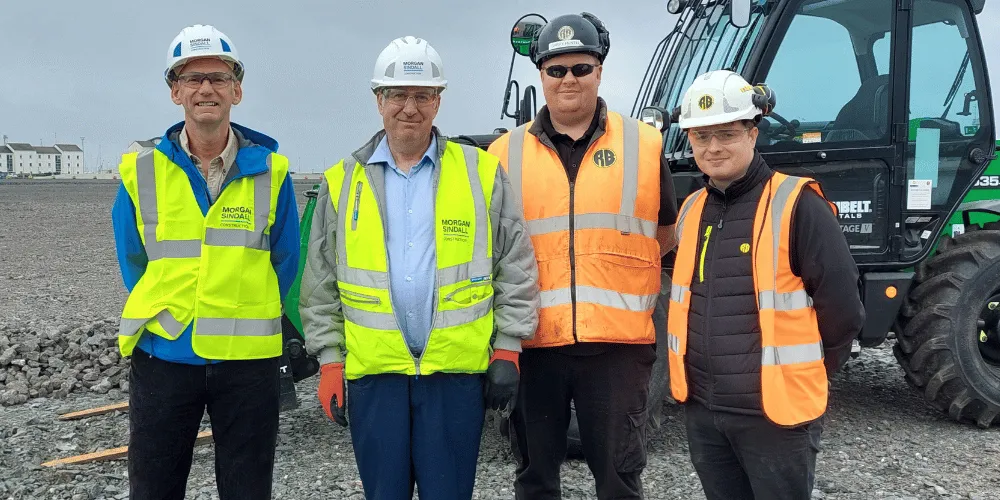 An image of four people wearing high-visibility vests in front of a piece of heavy machinery